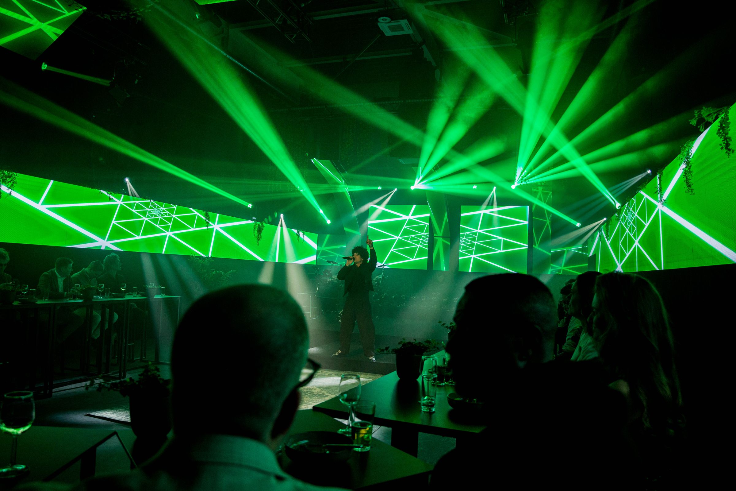 Artiest op een dinershow tussen LED-wanden en groene lichtbundels